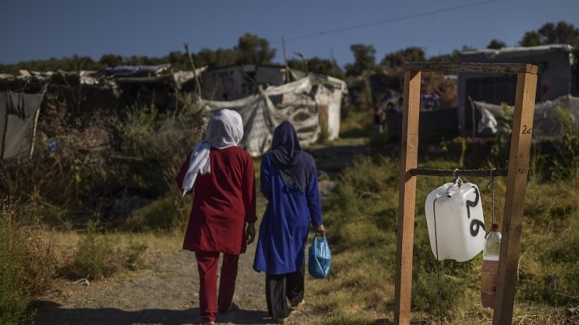 Two women walk past a plastic container of hand sanitizer at the refugee camp of Moria, in the island of Lesbos on August 24, 2020. 