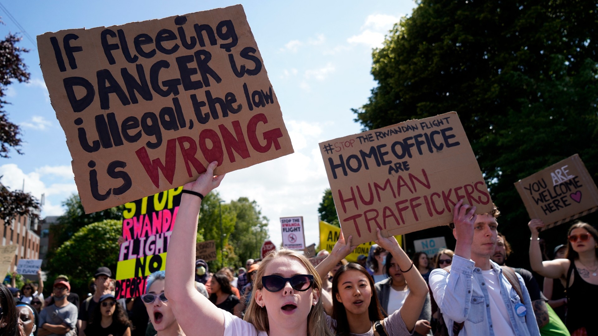 Protesters hold up placards as they gather close to the Brook House immigration removal centre beside Gatwick Airport, south of London on 12 June 2022 (AFP) 