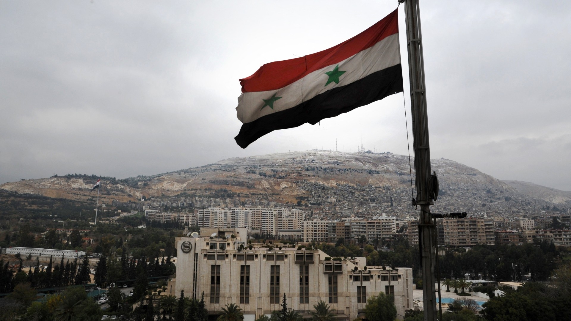 A Syrian flag flutters in the foreground with Damascus' Sheraton hotel (C) and Mount Qasyun in the background on 12 December 2013 (AFP)