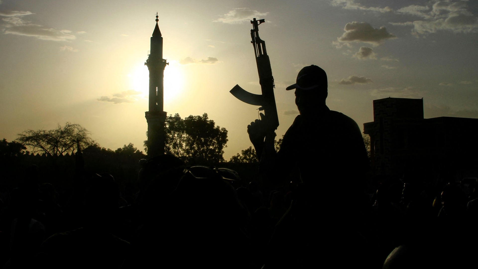 A fighter loyal to Sudan's army chief Abdel Fattah al-Burhan holds up a weapon backdropped by the minaret of a mosque, in the southeastern Gedaref state on 27 May 2024 (AFP)