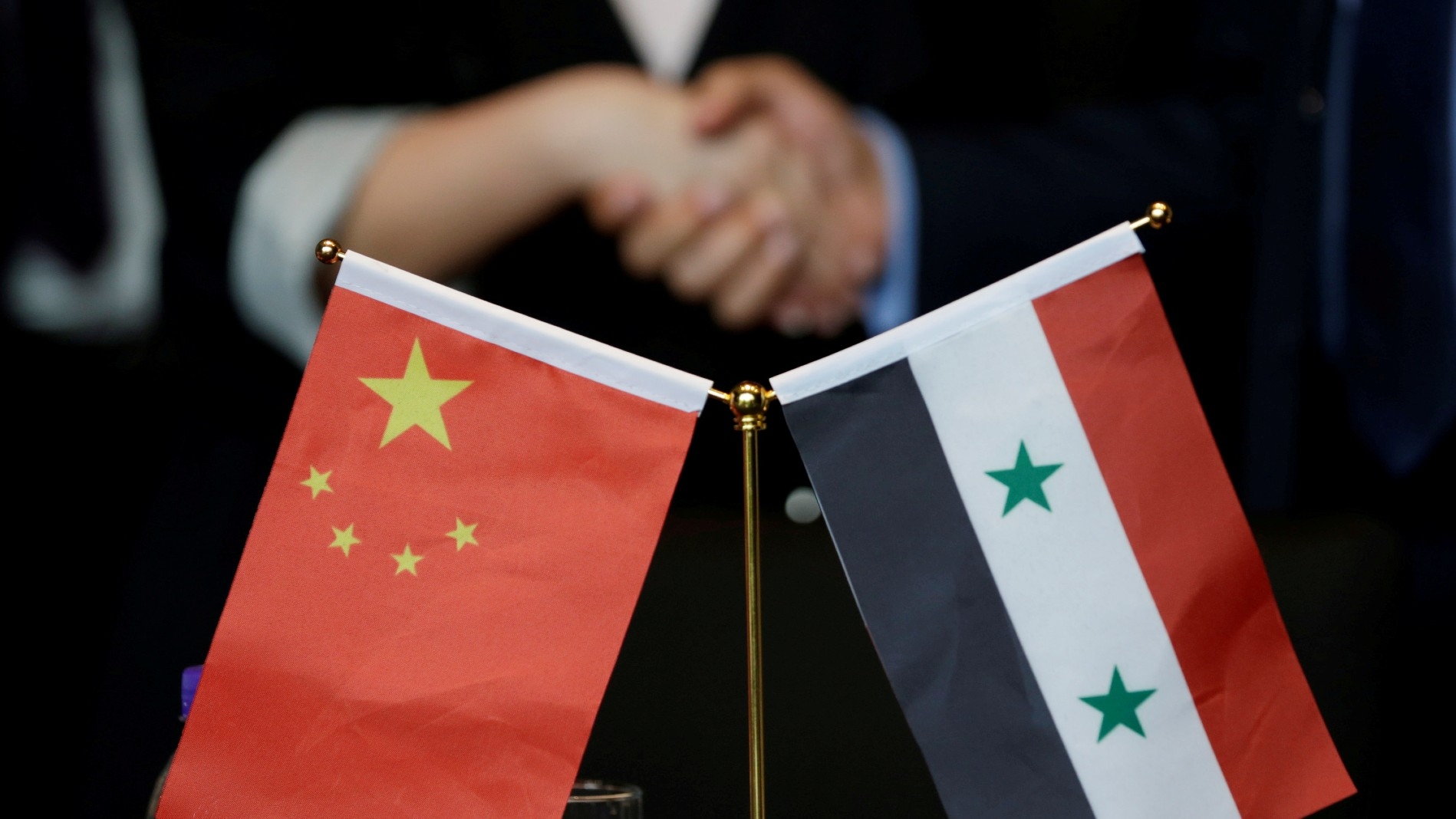 Chinese and Syrian businessmen shake hands behind their national flags during a meeting to discuss reconstruction projects in Syria, Beijing, China on 8 May, 2017 (Reuters)