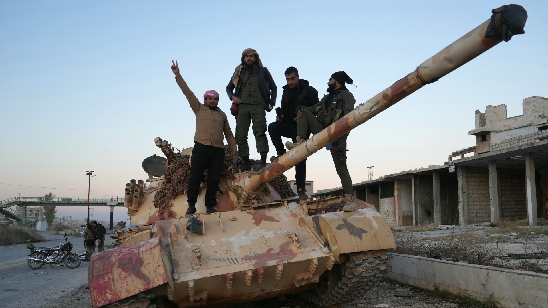 Fighters pose for a picture on a tank on the road leading to Maaret al-Numan in Syria's northwestern Idlib province on 30 November (Muhammad Haj Kadour/AFP)