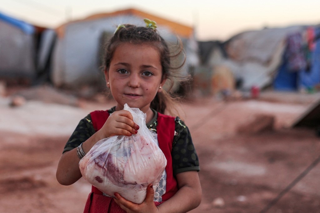 Une petite Syrienne se promène avec un paquet de viande fraîchement découpée, distribué par des volontaires, à l’occasion de l’Aïd al-Adha, dans un camp pour Syriens déplacés, dans la province d'Idleb, le 10 juillet 2022 (AFP/Aaref Watad)