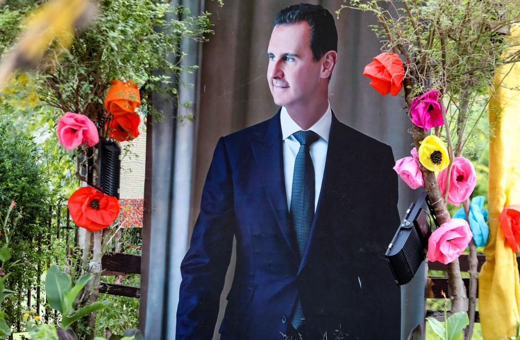 Un poster de Bachar al-Assad décoré avec des fleurs en papier, à Damas, le 22 juin 2022 (AFP/Louai Beshara)