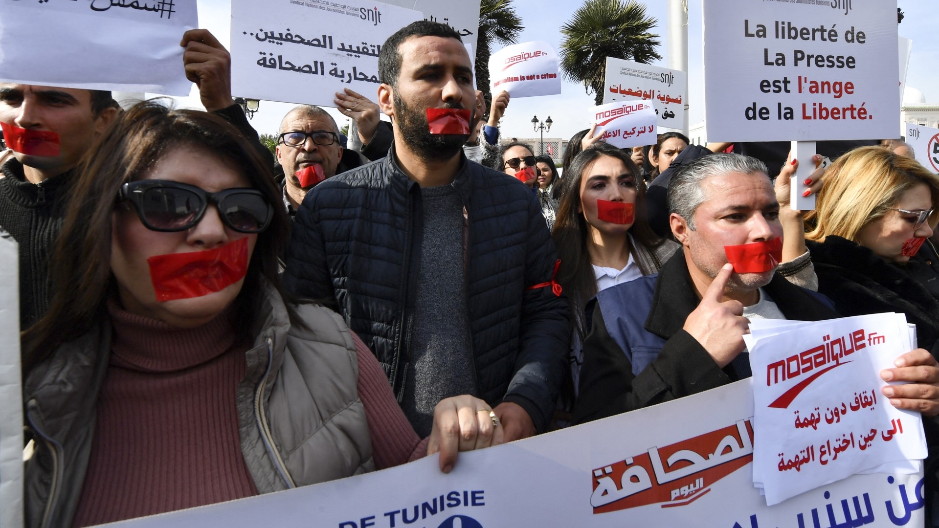 Tunisian journalists cover their mouths with red tape as they protest in front of the Prime Minister's office in the capital Tunis on 16 February 2023 (AFP)