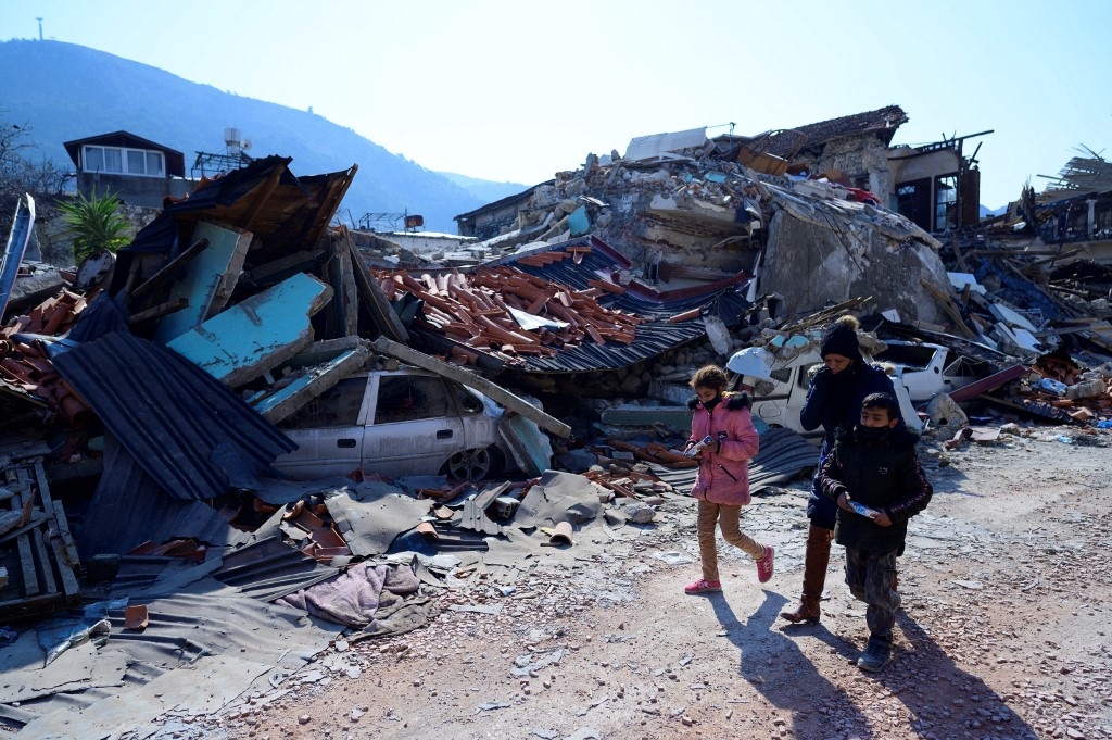 Des rescapés marchent à côté des ruines causées par le puissant séisme à Antakya, au sud de la Turquie (AFP/Yasin Akgul)