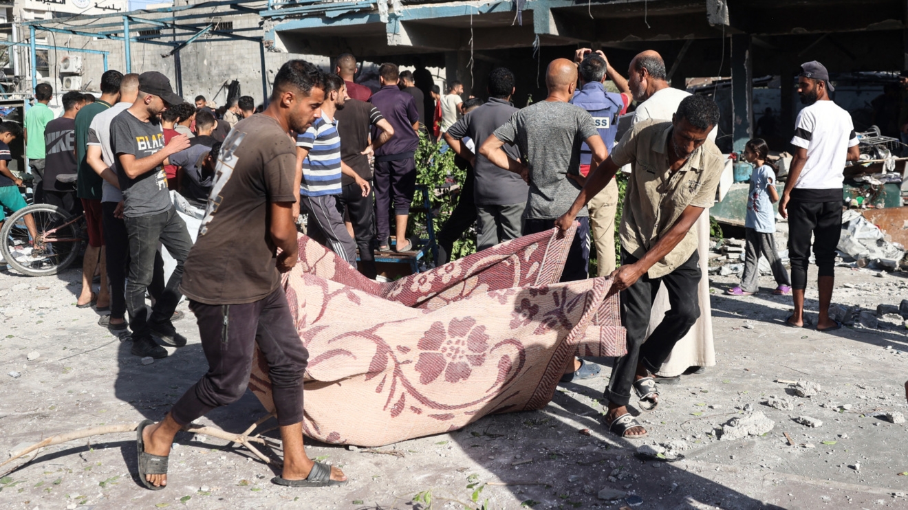 Palestinians use a blanket to carry a victim after an Israeli air strike hit al-Jawni school in the Nuseirat refugee camp, central Gaza, on 11 September (AFP/Eyab Baba)