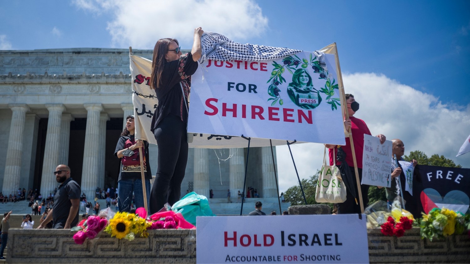 A woman drapes a keffiyeh on a banner calling for justice for Shireen Abu Akleh during a rally in Washington, DC on 15 May 2022.