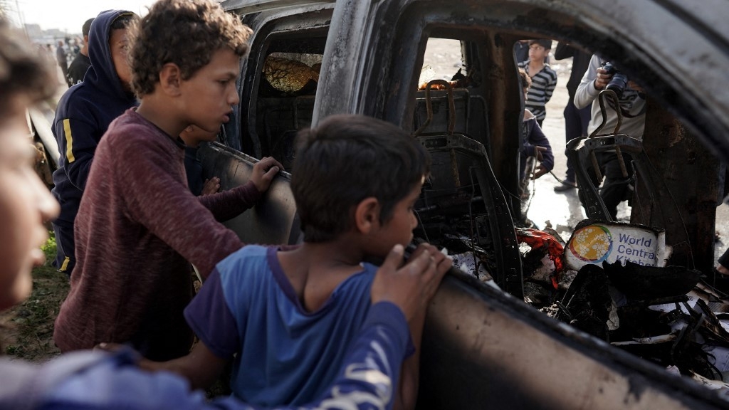 People gather around the carcass of a car used by US-based aid group World Central Kitchen, that was hit by an Israeli strike the previous day in Deir al-Balah in the central Gaza Strip on 2 April 2024 (AFP)