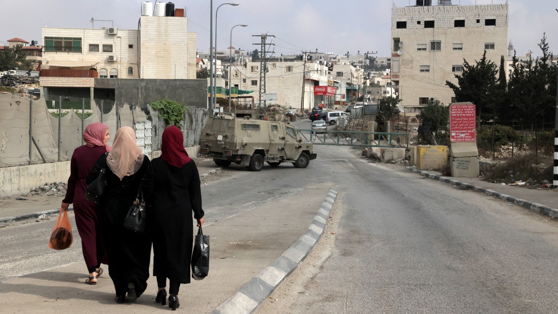 Palestinian women walk toward Israeli security forces manning a checkpoint blocking an entrance to the occupied-West Bank city of Hebron on 30 October 2022 (AFP)