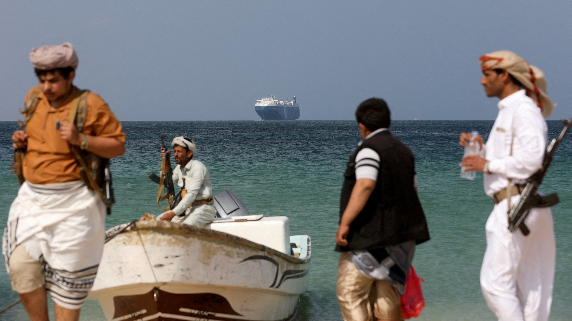 Armed men stand on the beach as the Galaxy Leader commercial ship, seized by Yemen's Houthis last month, is anchored off the coast of al-Salif, Yemen, on 5 December 2023 (Reuters/Khaled Abdullah)