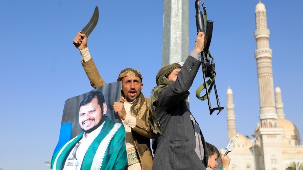 Houthi fighters, one holding a portrait of leader Abdul Malik al-Houthi (L), brandish their weapons during a protest following US and British forces strikes, in the Houthi-controlled capital Sanaa on 12 January 2024 (AFP)