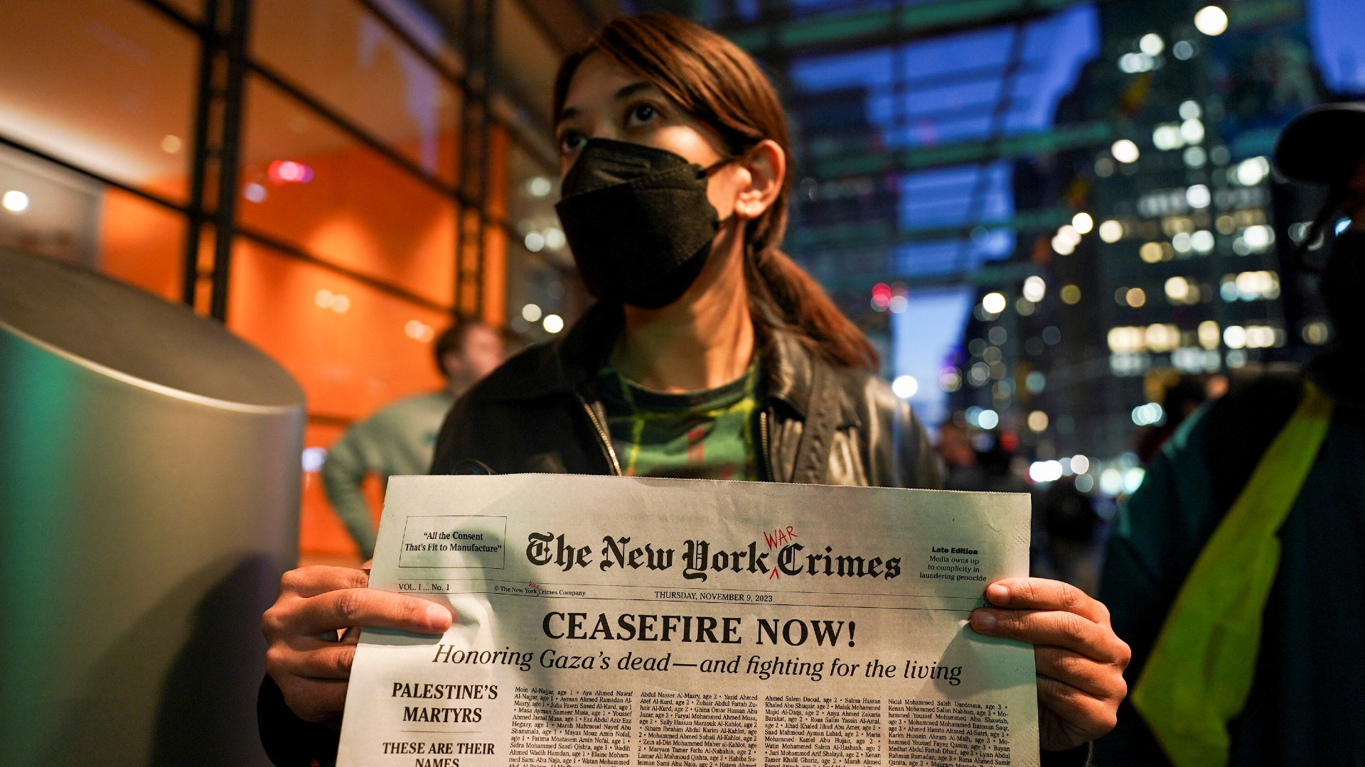 A woman holds a mock-up newspaper with a list of names of people killed in Gaza during a rally in support of Palestinians outside The New York Times building in New York City, US, on 9 November 2023 (Reuters)