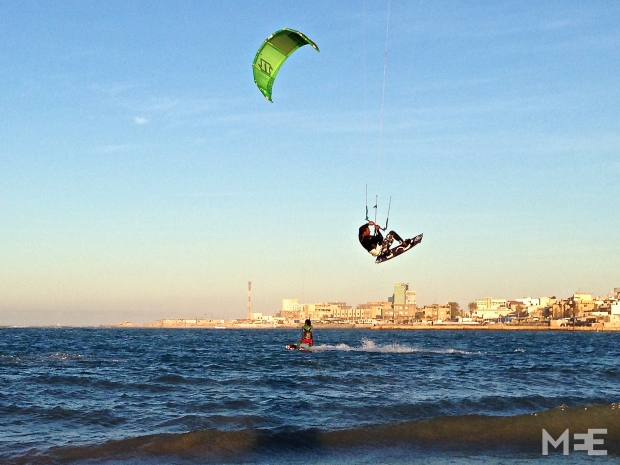 Jalal, one of the country’s more experienced kiters, performing a jump with Tripoli’s skyline in the background (MEE/Tom Wescott)