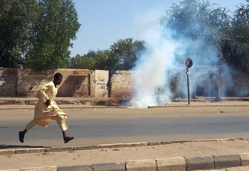 A man flees tear gas at a protest in Omdurman, Sudan, on 13 November 2021 (AFP)