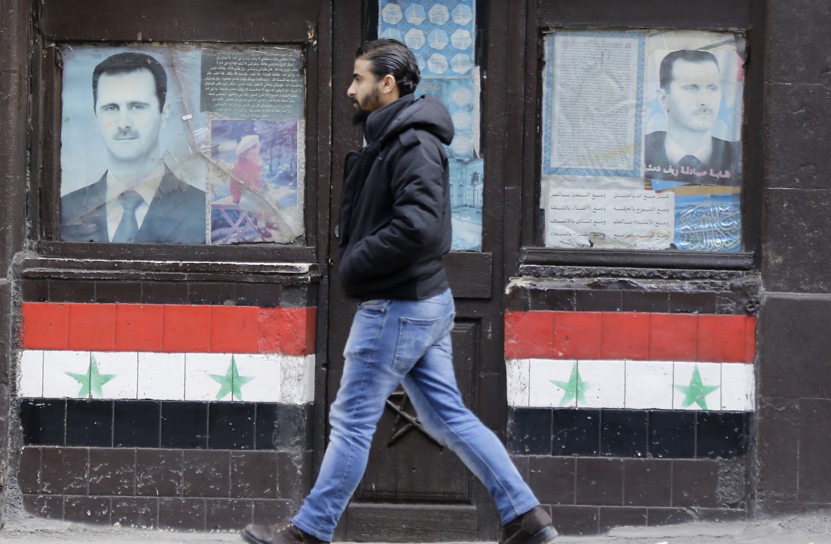 A Syrian man walks past posters of Syrian President Bashar al-Assad on a shop front in the capital Damascus on January 3, 2017 (AFP)