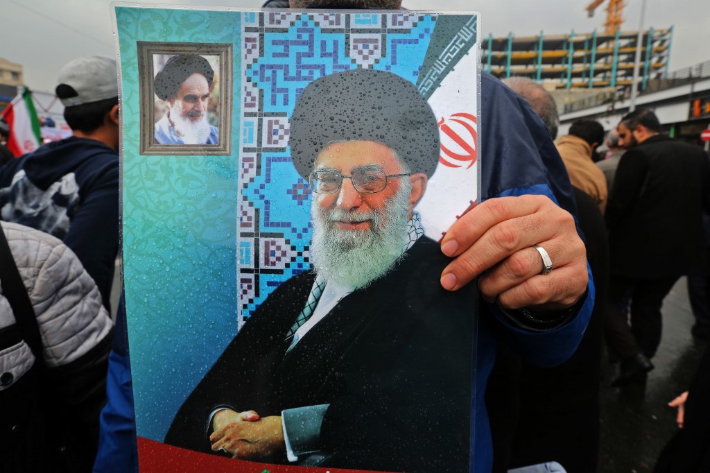 An Iranian holds up a portrait of Supreme Leader Ali Khamenei, with a smaller corner portrait of Ayatollah Khomeini, in Tehran on 11 February (AFP)