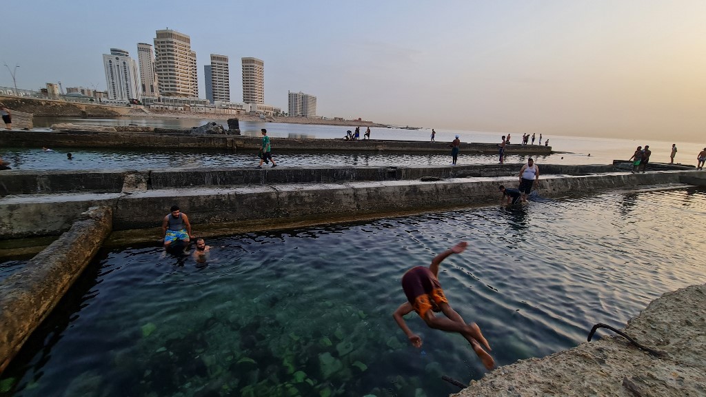 Youths jump in the Mediterranean sea water near the Dhat El Emad (Of the Pillars) Tower complex at sunset in Libya's capital Tripoli on 28 June 2021 (AFP)