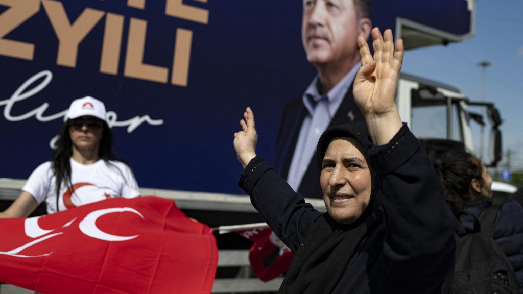 A woman waves in front of a campaign truck bearing Erdogan’s portrait in Istanbul on 22 May 2023 (AFP)