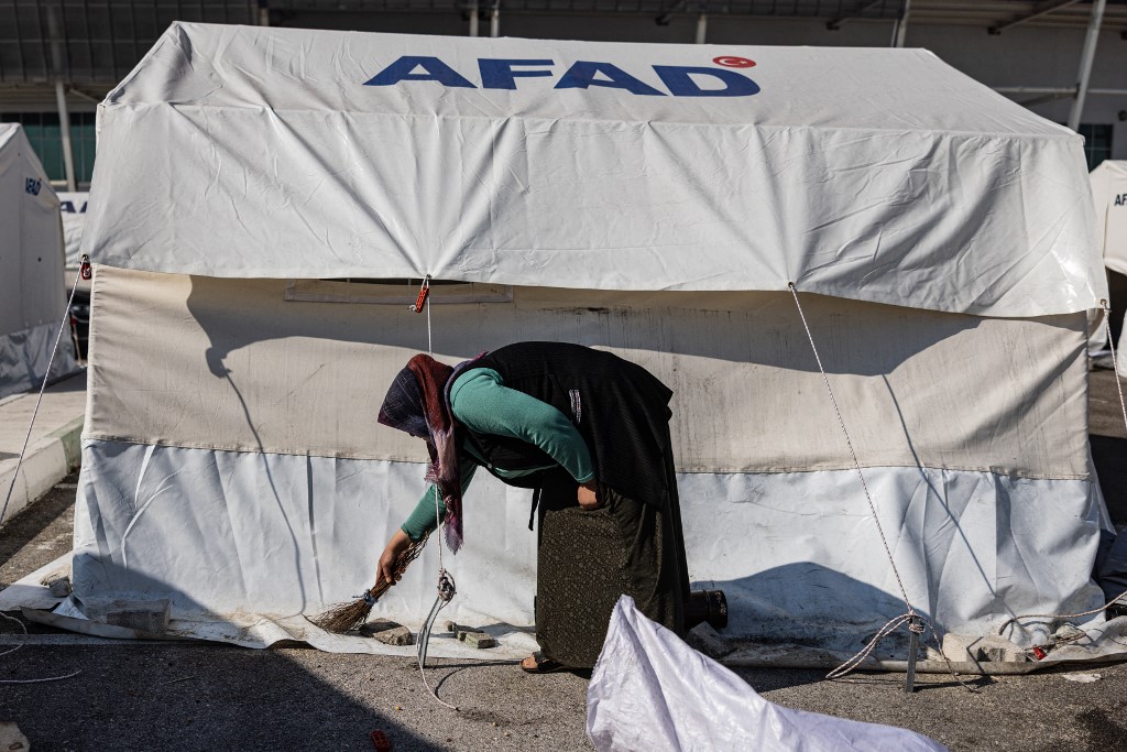 Une femme balaie autour de sa tente dans un camp de fortune à côté du nouveau stade Hatay à Antakya, dans le sud de la Turquie, le 22 février 2023 (AFP/Samir al-Doumy)