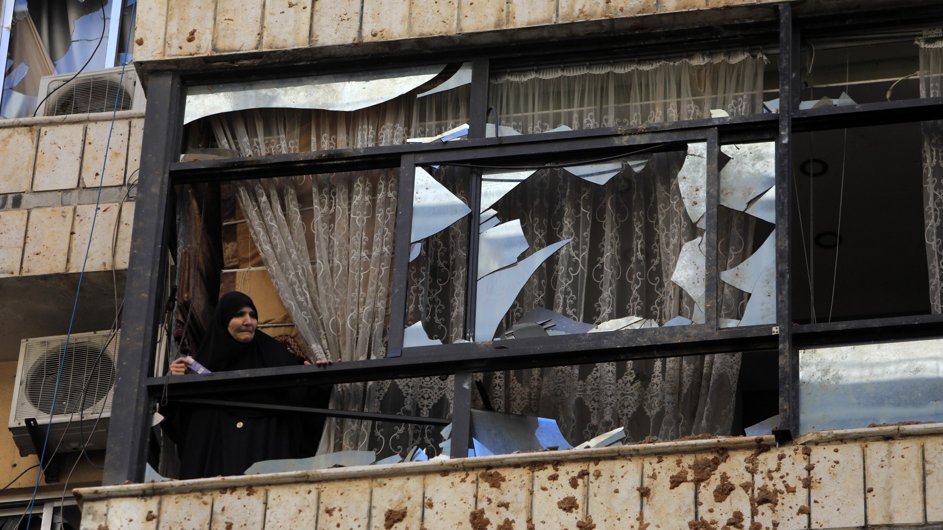 ​  A woman watches from a broken window near a building targeted by an Israeli strike in Beirut's southern suburbs on 20 September (AFP)  ​